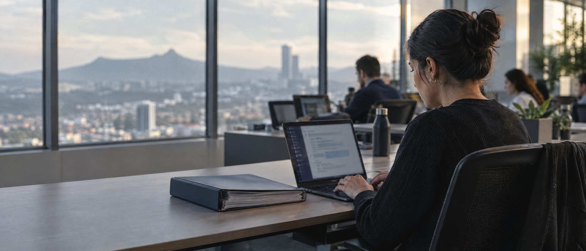 An employee typing a question on a laptop beside a binder of policies