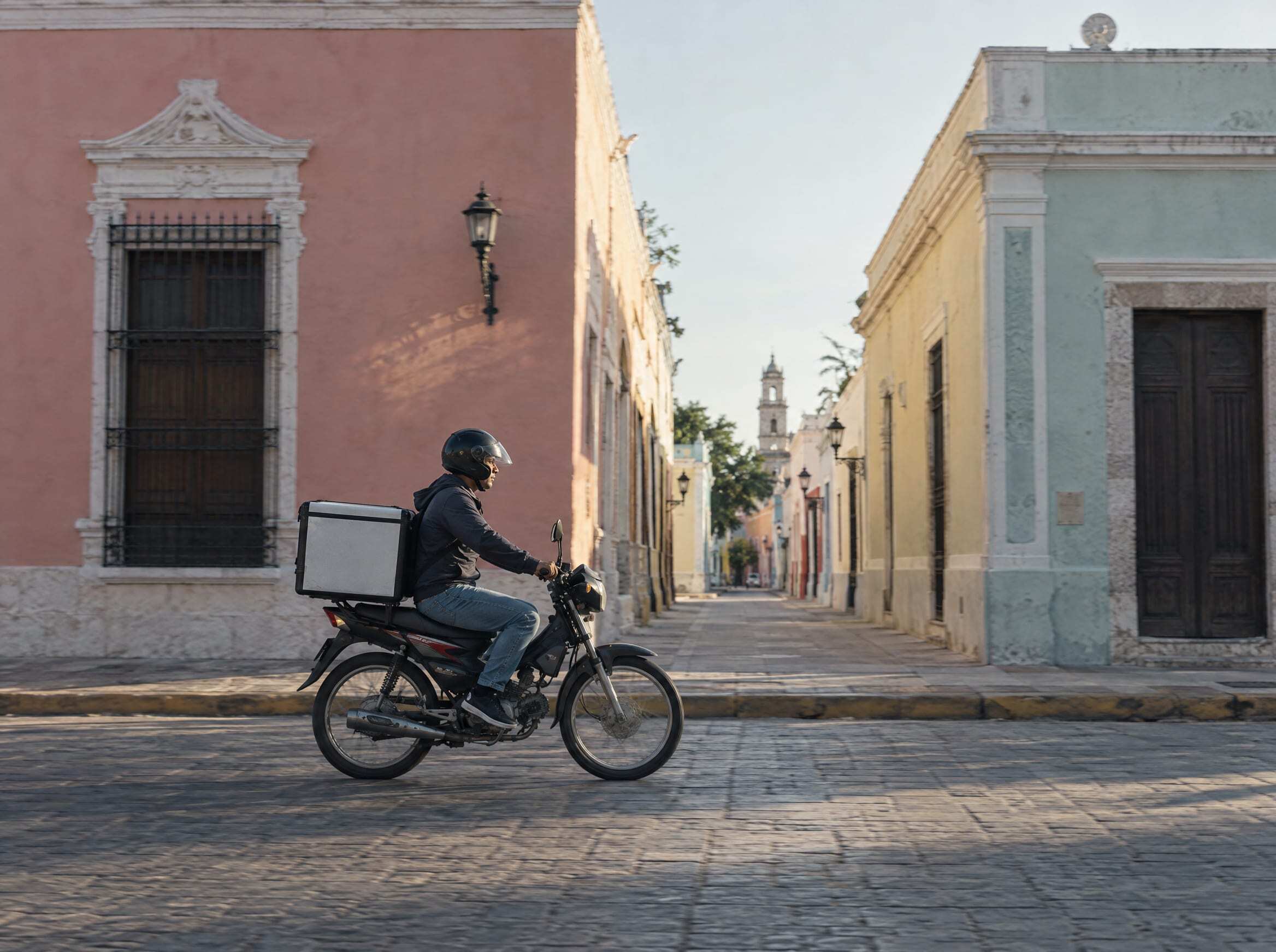 Un repartidor en motocicleta por una calle colonial de Mérida