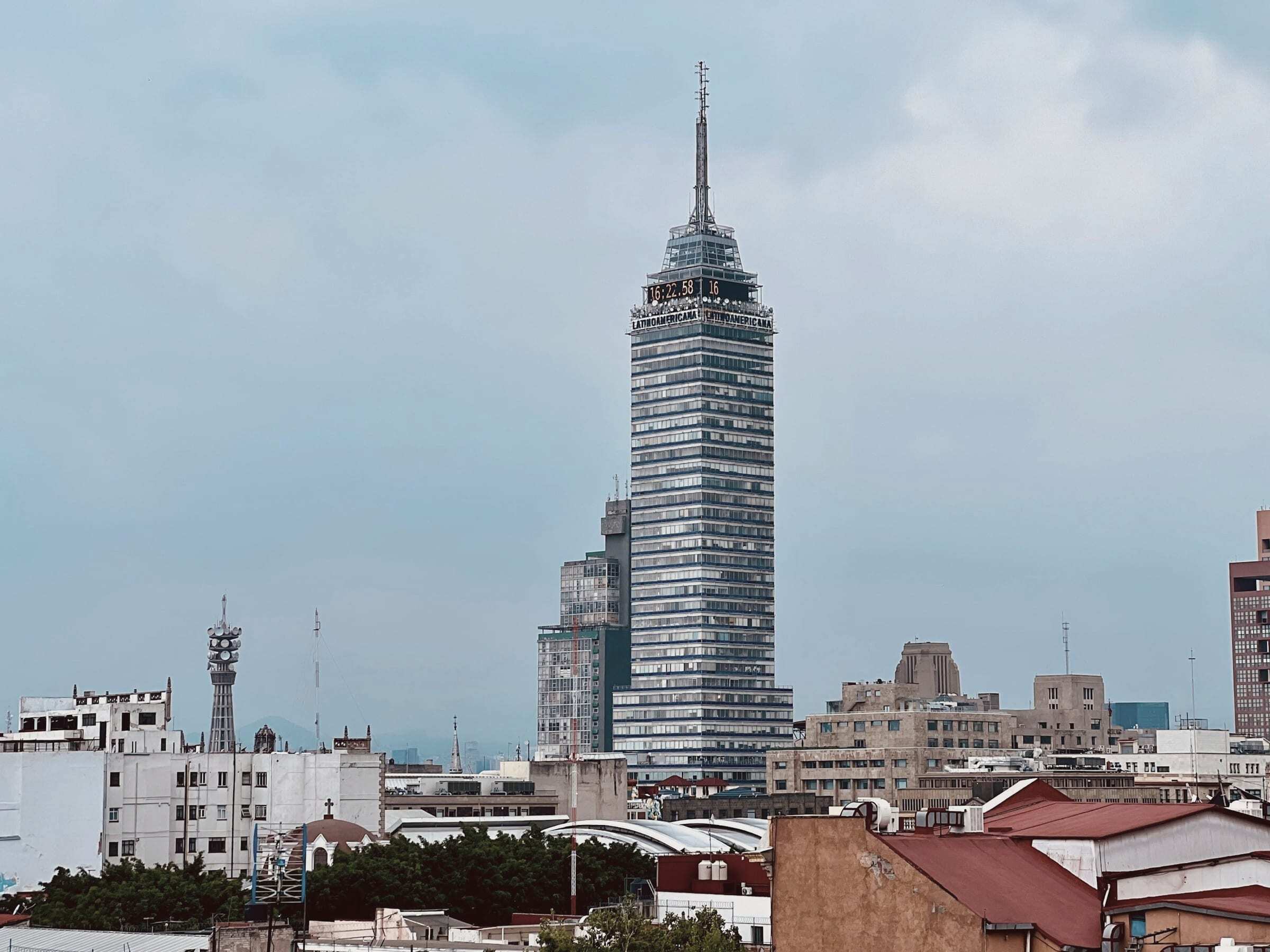 Torre Latinoamericana rising above rooftops in central Mexico City under a pale blue sky