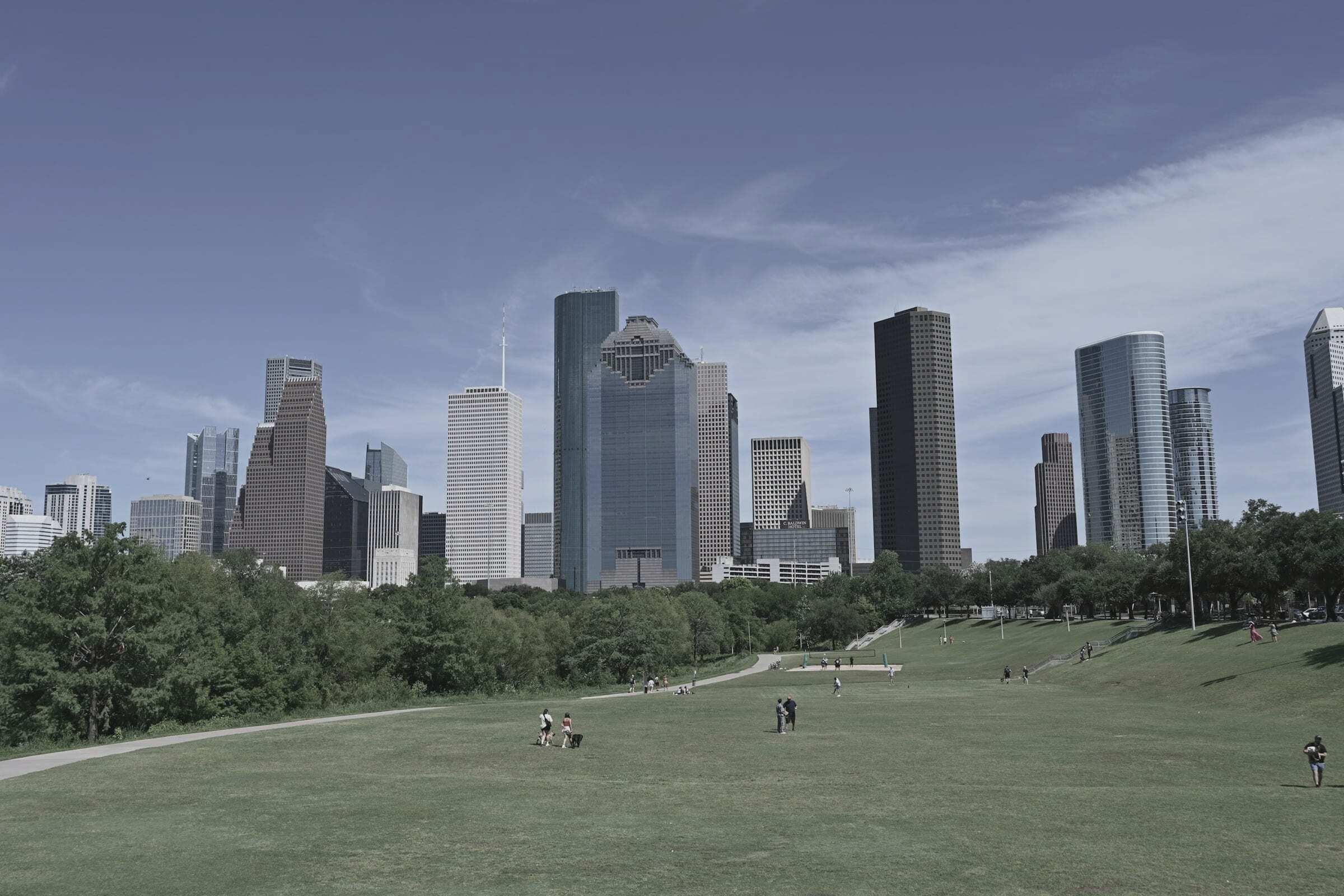 Downtown Houston skyline behind a wide grassy park under a clear blue sky