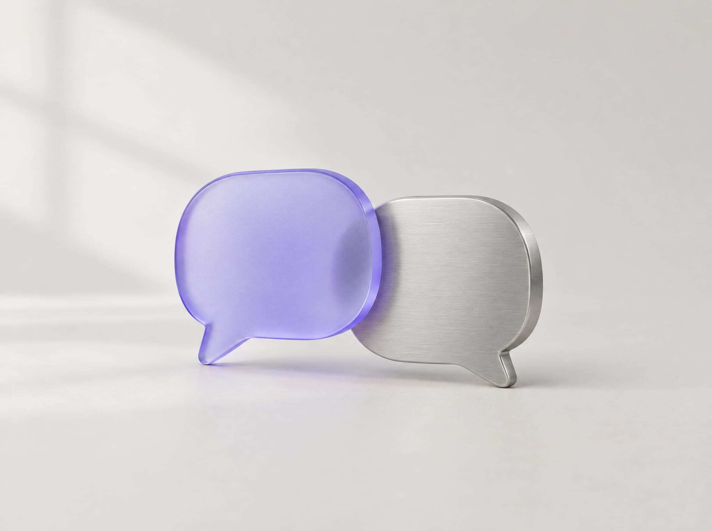 Two speech bubbles, one of violet frosted glass and one of brushed aluminum